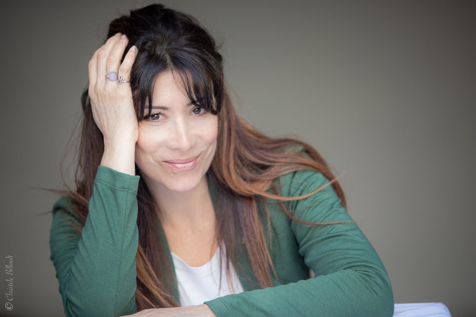 Portrait de Flor Lurienne, veste verte, la main dans les cheveux